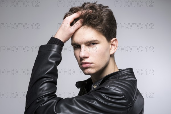 Young fashion man passing his hand through his hair. Male fashion model with hand in hair. Man Hair Beauty. Handsome Male Model Touching Healthy Hair. Stylish guy posing on grey background