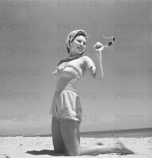 1940s summer. A young woman by the sea is getting a nice suntan. She is wearing a typical 1940s bathing suit and a scarf on her hair. Photo Kristoffersson Ref AR79-6. Sweden 1947