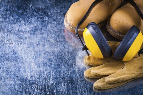 Leather waterproof boots protective gloves and noise reduction ear muffs on scratched metallic surface construction concept