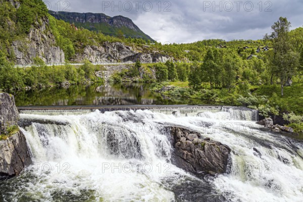 Magnificent seething waterfall - threshold on the river Bioreio. The river flows in western Norway. The green shores are reflected in the smooth water to the edge of the waterfall