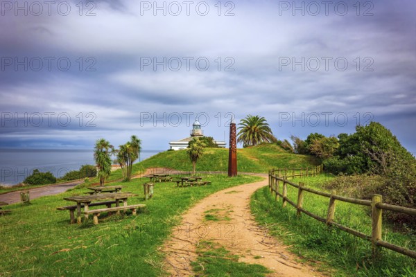 The road to the lighthouse. The picturesque seaside fishing town of Candas. Atlantic coast, Spain. Part of the famous Costa Verde beach. Snow-white lighthouse over the cliff