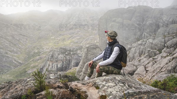 Young woman in sports clothing sitting on rocks enjoying the scenery of Andringitra national park, large stones massif background, during hike to pic Boby peak, Andringitra National Park, Madagascar