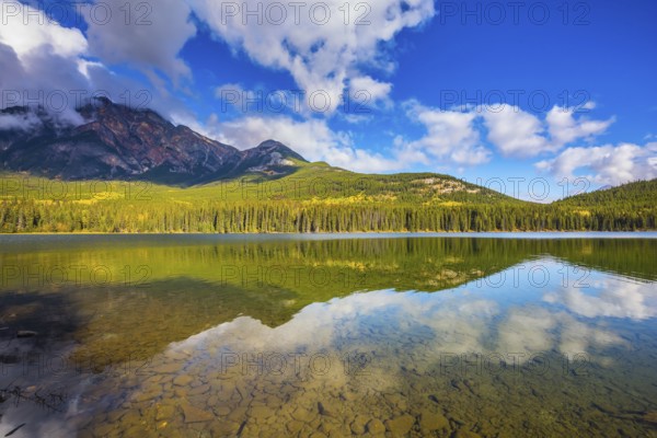 Frosty morning in the Rocky Mountains, Canada. Clear water Pyramid Lake reflects the clouds and pine forests on the shore