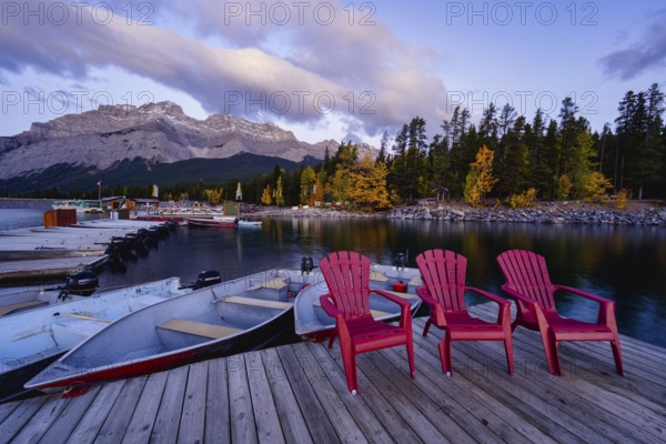 Beautiful autumn landscape scene in lake and mountain in background in west Canada, colour kayaks and canoes and small boats Three red plastic chairs