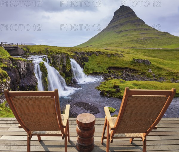 Threaded full-flowing waterfall Kirkyufell Foss on the grassy mountains. Deck chairs on the wooden floor waiting for tourists