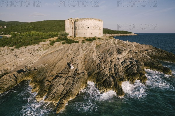 Bride and groom stand on the rocks near the fortress by the sea. Aerial view.