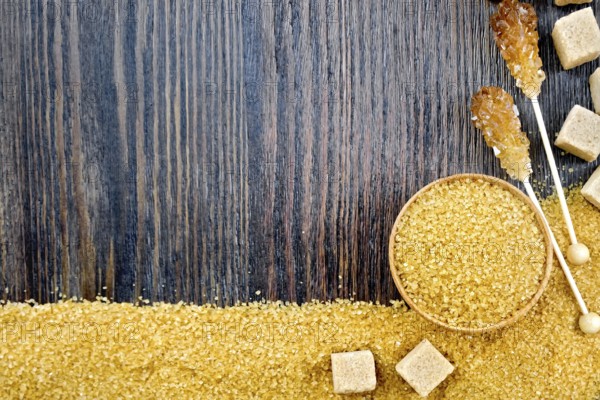 Sugar brown granules in a bowl, cubes and crystals on a stick in the form of a frame on the background of a wooden board