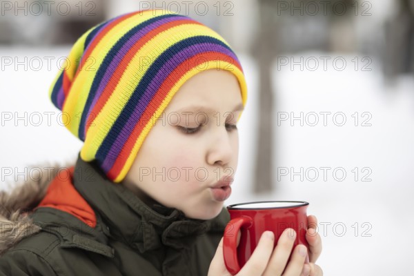 Glückliches Kind Kind Teenager Junge hält roten Becher mit heißem Kakao, Schokolade oder Tee und trinken. Kinder Aktivität im Winter Tag. Urlaub Urlaub Konzept