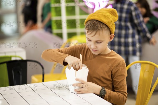 Kid teen child boy eating ramen noodle wok with chopsticks in food court. Lunch time