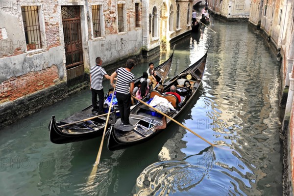 Venice, Veneto, Italy, Europe, Gondolas manoeuvre through a narrow canal, surrounded by old brick buildings