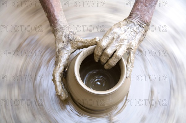Pottery, artist muddy hands making clay pot giving shape on spinning wheel, semi urban village Dilwara, Udaipur, Rajasthan, India