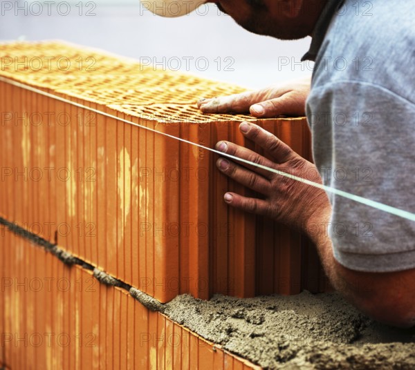 Anonymous construction worker on a building site erecting a brick wall. Brick wall of a solid house. Symbolic image of illegal labour and bungling Austria