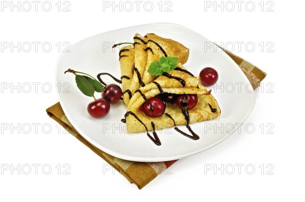 Two pancakes with berries cherries, mint, chocolate icing on a white plate and napkin isolated on white background