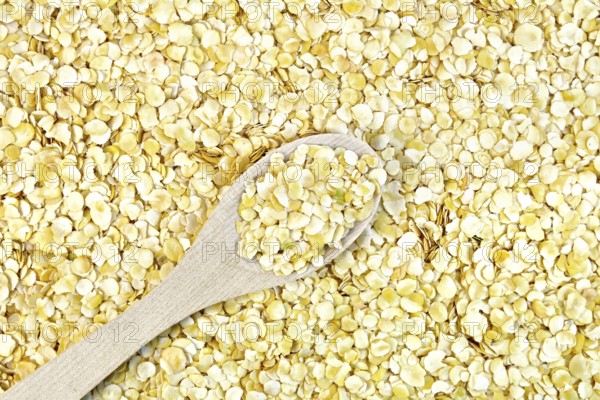 Texture of yellow pea flakes with a wooden spoon