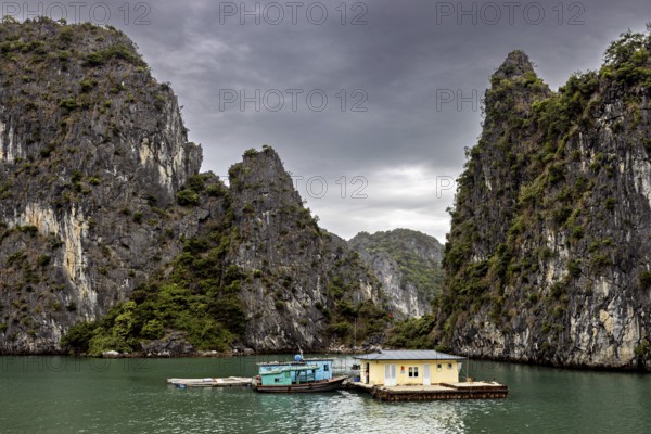 Single houseboat between towering limestone cliffs under a grey sky, The floating villages in Halong Bay in Vietnam