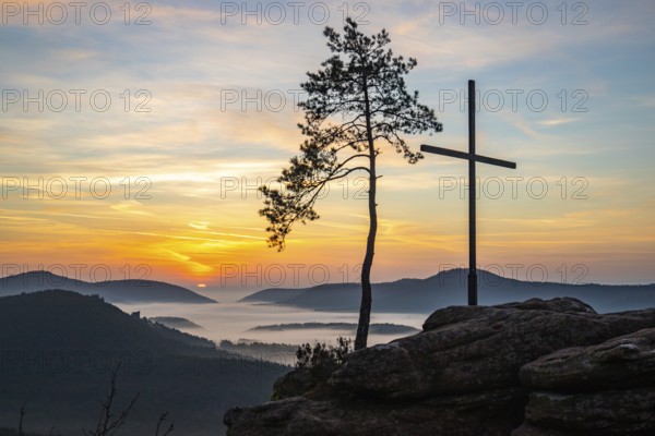 Landscape shot of nature in the morning. Mist in the valley and a summit cross on a sandstone cliff. Sunrise in the Palatinate Forest, Germany