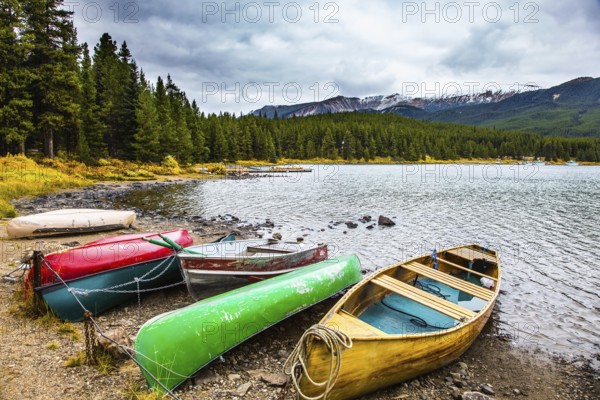 Multicolored boats and canoes dry on the lakeside. Cold cloudy fall day in the Canadian Rockies. Lake Maligne in the snow-capped mountains is surrounded by coniferous evergreen forests