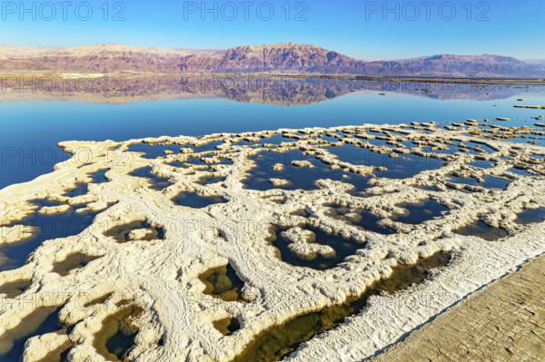 Evaporated salt forms bizarre patterns on the water. Dead Sea. The blue water is surrounded by pink mountains. Sunny winter day. The picture was taken by a drone from a aerial view. Israel