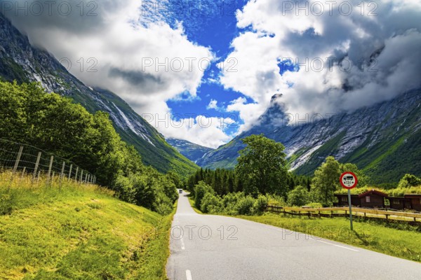 Scenic road in the mountains. Wonderful fresh green vegetation and lush snow-white clouds. Travel to fabulous Scandinavia. Norway