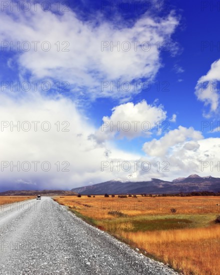 The dirt road in the endless pampas. Strong wind drives the clouds. See the mountains on the horizon