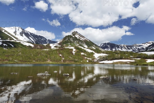 Summer landscape of Kamchatka: view of Mountain Range Vachkazhets and clouds in blue sky, reflection in mountain lake on sunny day. Eurasia, Russian Far East, Kamchatka Peninsula