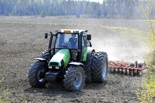 Farmer cultivating field with green Deutz-Fahr Agrotron 135 tractor and Vaderstad NZ aggressive tine harrow in the spring. Salo, Finland. May 13, 2021
