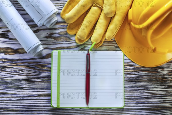 Blueprints notepad pen building helmet safety gloves on vintage wooden board