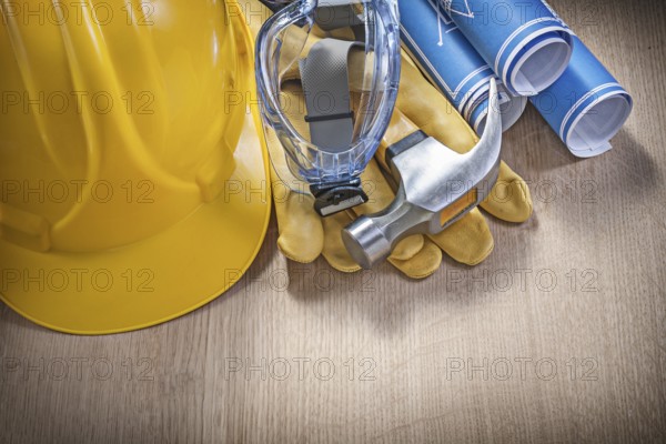 Protective work wear claw hammer rolled construction plans on wooden board