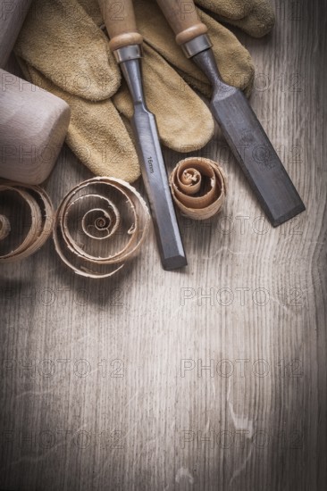 Wooden mallet curled up shavings flat chisels leather gloves on wood board vertical view construction concept
