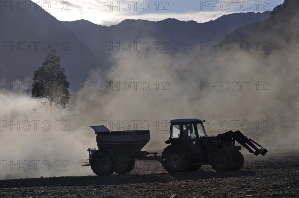 Tractor spreading lime with a fertiliser spreader, West Coast, New Zealand
