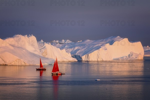 Large glaciers in the bay by the rocky shore in the light of the setting sun with fog over the water with red boat