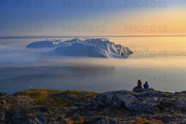 Large glaciers in the bay by the rocky shore in the light of the setting sun with fog over the water