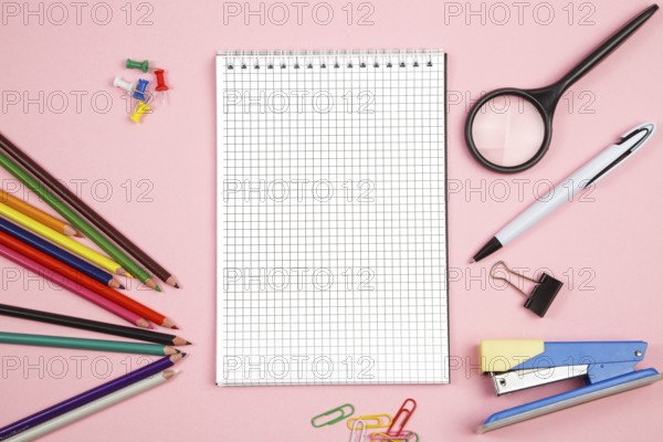 Colored pencils, stationery, paper notebook with pen and magnifier on pink isolated background. top view. flat lay. mockup