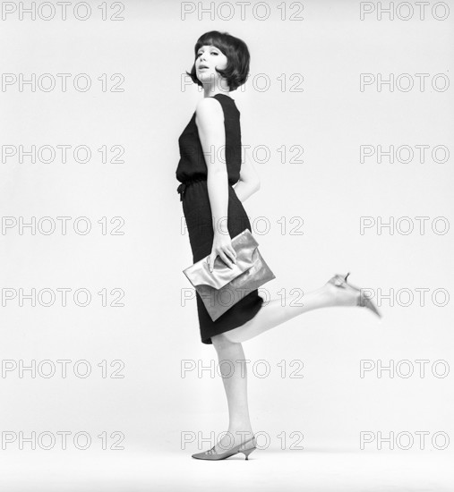 In the 1960s. A model in a typical 1960s outfit photographed in a studio. A black popular dress in the timely height just below kneeheight. Sweden 1960s Kristoffersson ref CV21-9