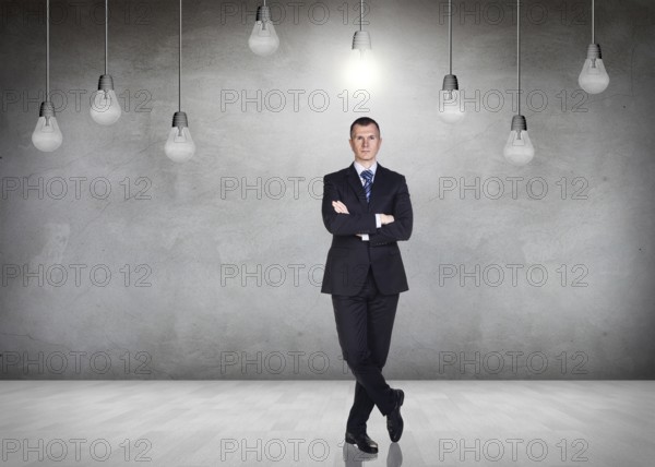 Businessman stands in a gray room with hanging bulbs