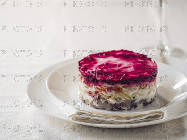 Layered salad herring under fur coat on table. Portion of traditional russian salad with herring, beet and other vegetables on white linen tablecloth. Copy space