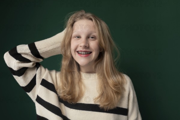 A woman with blonde hair is standing, wearing a striped sweater. She appears calm and is looking ahead. Her outfit consists of a striped sweater that complements her hair color