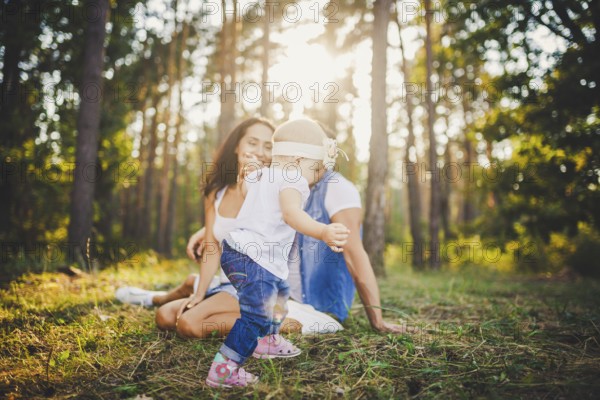 Young parents are taught to walk a daughter of one year on nature in a park on a lawn. The first steps of the child's hand with his mother and father