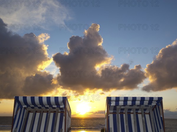 Two empty beach chairs enjoy the view of a golden sunset, norderney, north sea, germany