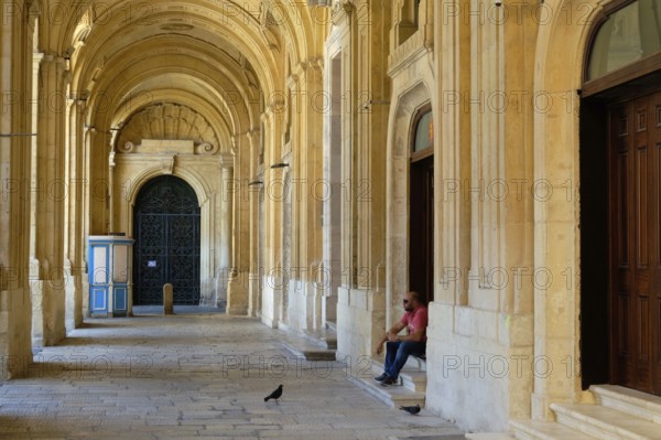 A man with his sandwich and two hungry pigeons in the archway of the National Library, Valletta, Malta
