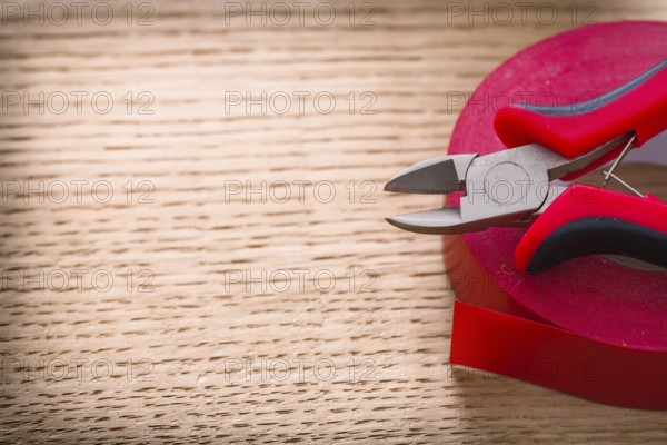 Red nippers and insulating tape on wooden board
