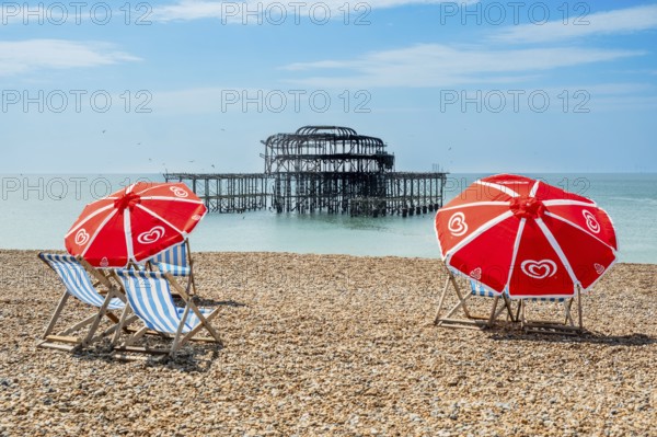 Folding chairs with parasols on the beach in front of the ruins of the burnt down West Pier in Brighton, East Sussex, England, Great Britain