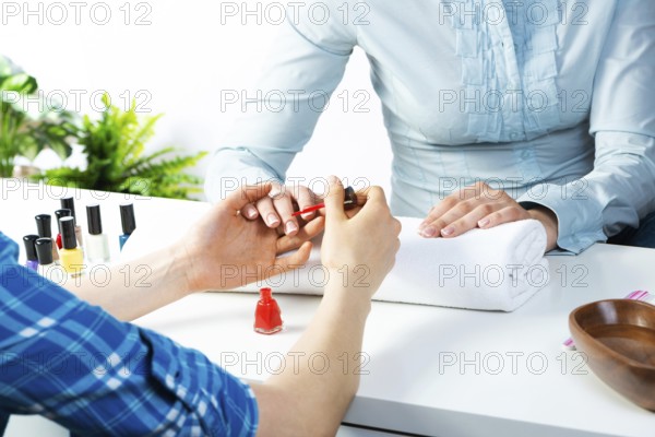 Manicurist working with client's nails at table. Closeup of beautiful female hands applying red nail polish in beauty salon. Professional nail care and beautician procedure in beauty center