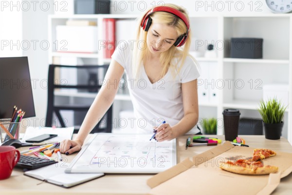 Beautiful blonde girl in a white tank top and dark pants. The girl listens to music through the red headphones and works with a marker and a magnetic board in a light cabinet. photo with depth of field