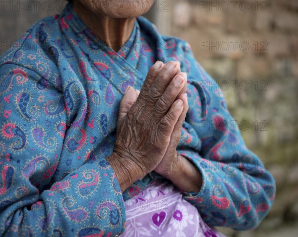 Unrecognized elder nepalise woman wearing blue cloths crossing her wrinkled hands