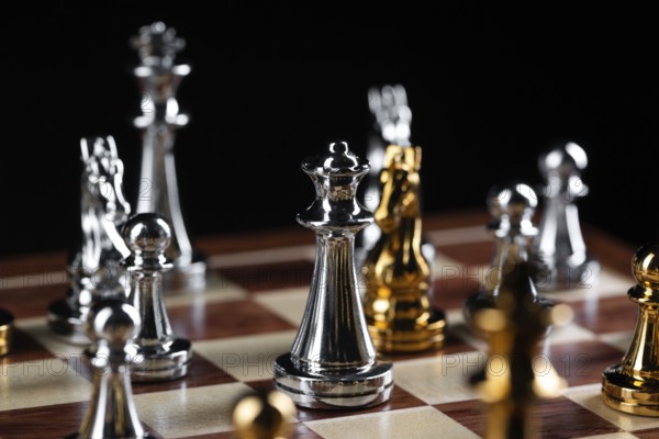 Gold and silver chess figures placed on wooden chessboard. Intellectual duel and tactical battle in business. Strategy planning, leadership and teamwork concept. Close-up metal chess pieces on board