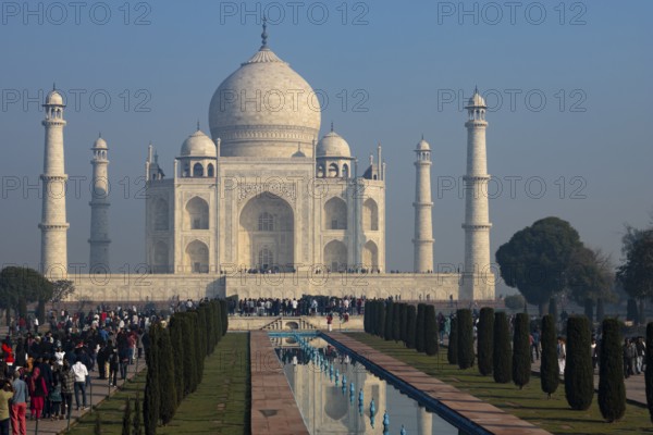 Taj Mahal, the mausoleum built for Mumtaz Mahal by her husband, the Mughal emperor Shah Jahan. Symbol of love, Wonder of the World, a UNESCO World Heritage Site, famous landmark and tourist attraction. View from the garden on a busy day with many people visiting the monument. Winter morning light, clear blue sky. Agra, Uttar Pradesh, India