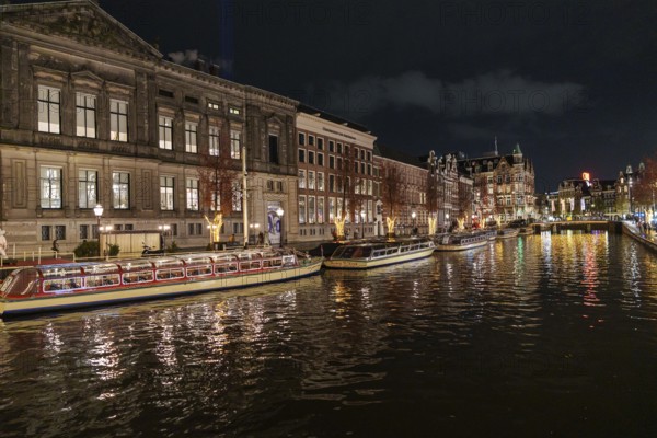 Illuminated boats and buildings are reflected in the canal water at night, Amsterdam, Netherlands