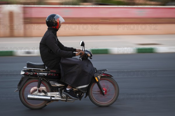 Marrakesh, MOROCCO - OCTOBER 5, 2024: Moroccan man riding a scooter on the road. Blurred background due to panning