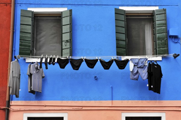 Venice, Veneto, Italy, Europe, Vibrant blue façade with green shutters, contrasting clothing on clothesline in foreground